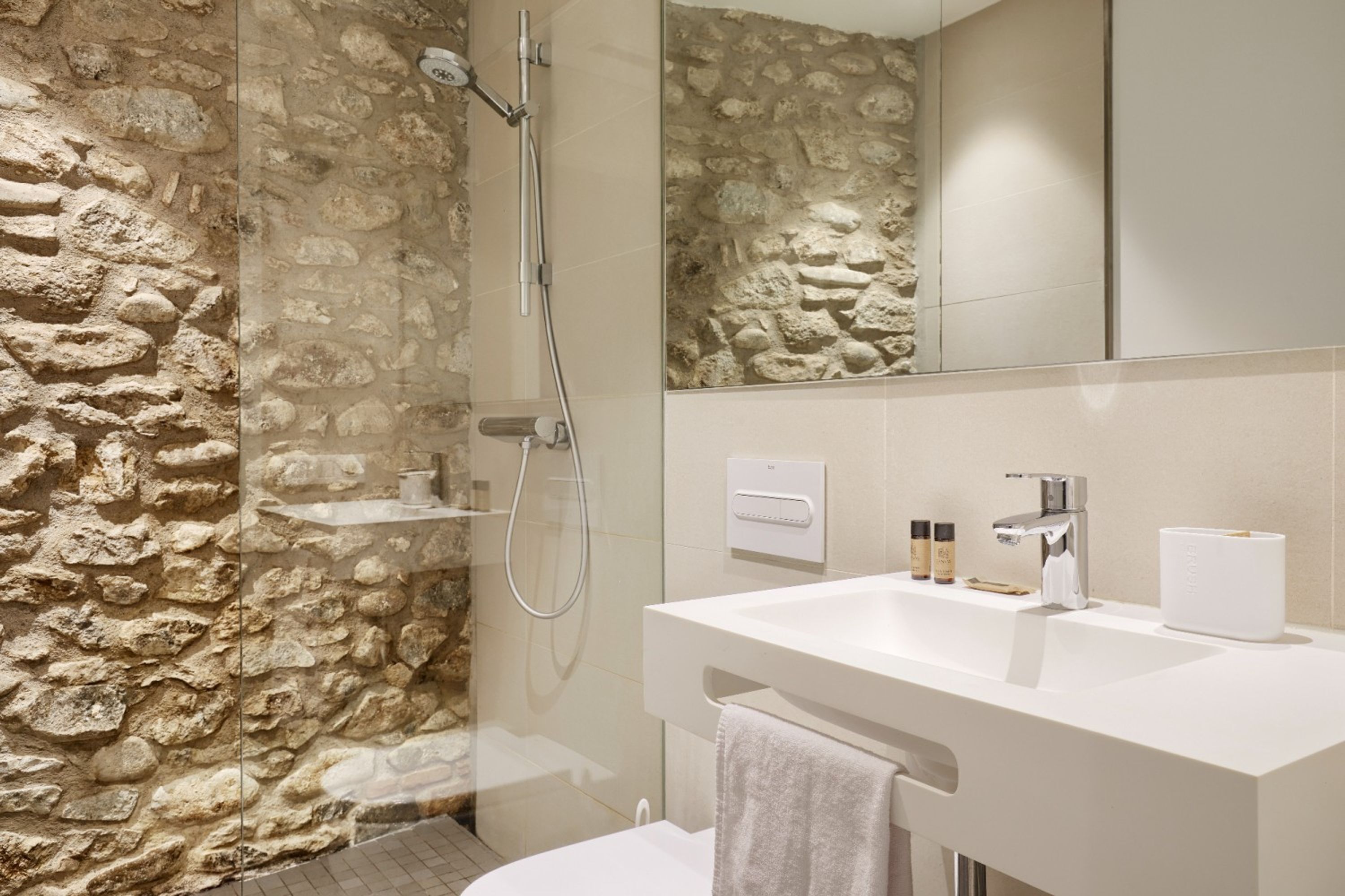 A bathroom with a stone wall, a shower, a sink, and a mirror.
