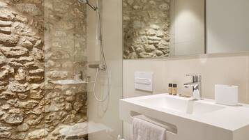 A bathroom with a stone wall, a shower, a sink, and a mirror.