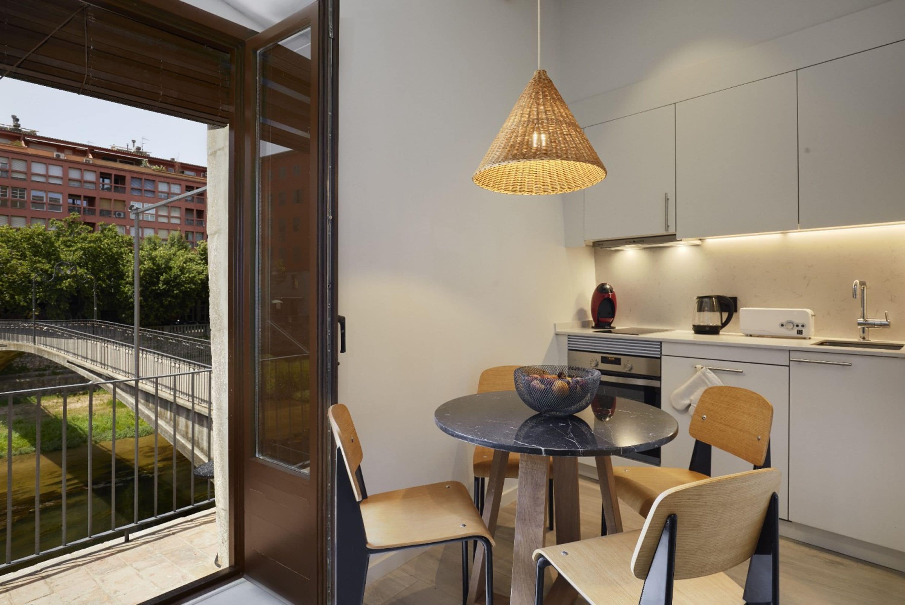 Una cocina moderna con comedor, una lámpara colgante y vistas a un puente y vegetación.