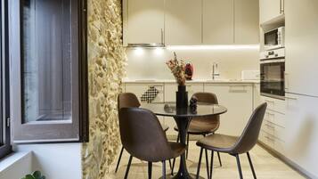 Una cocina moderna con gabinetes blancos, una mesa de comedor con sillas, una lámpara colgante y una pared decorativa de piedra.