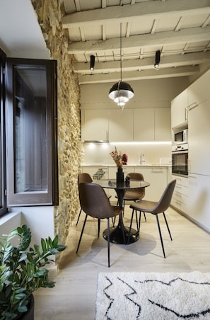 A modern kitchen with white cabinets, a dining table with chairs, a hanging light fixture, and a stone accent wall. - Casa Calma & Casa Canvas (Girona)