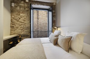 A bedroom with a stone wall, a bed with white bedding, a desk, and a chair. - Casa Calma & Casa Canvas (Girona)