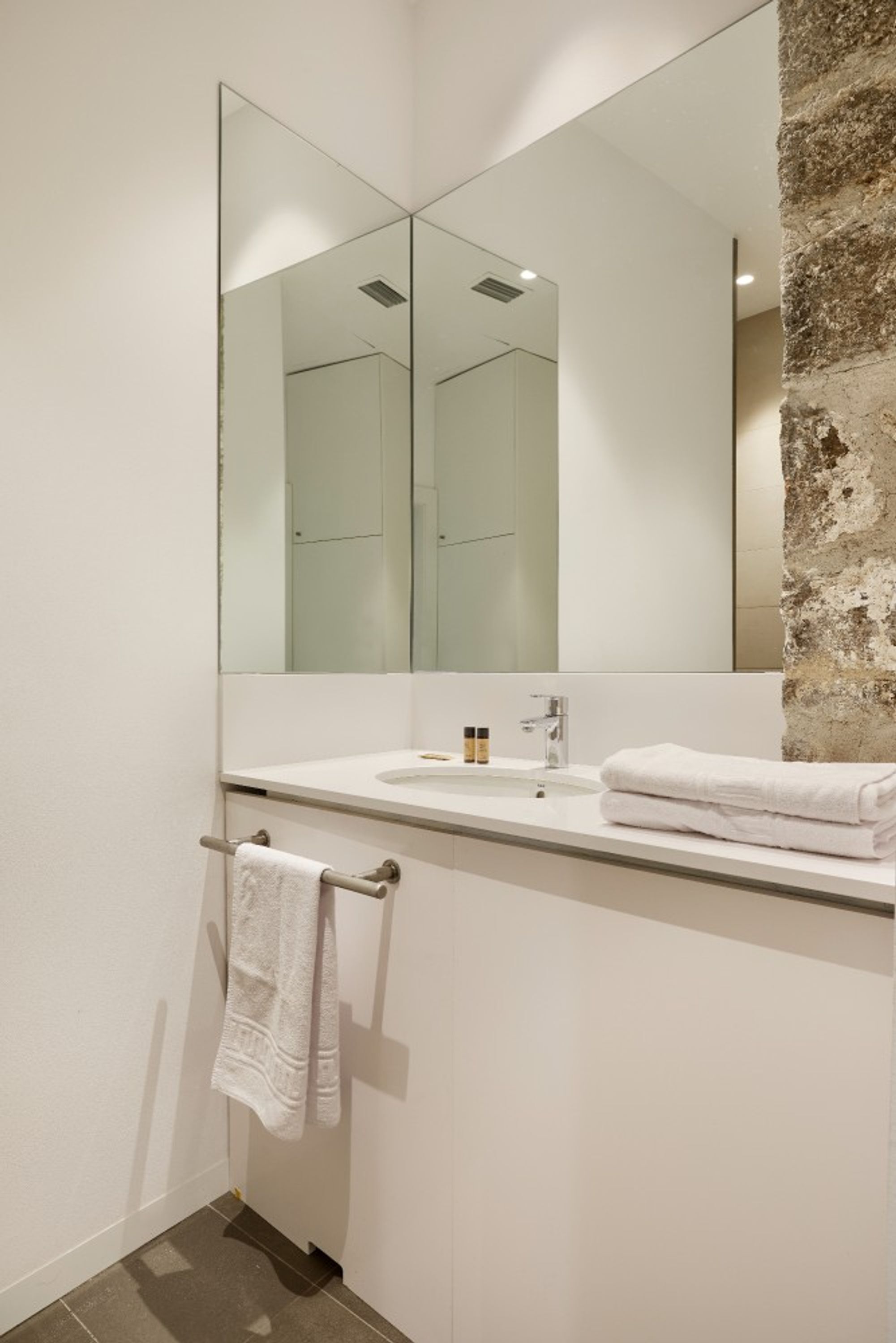 A bathroom with a large mirror, a sink, and a towel rack.