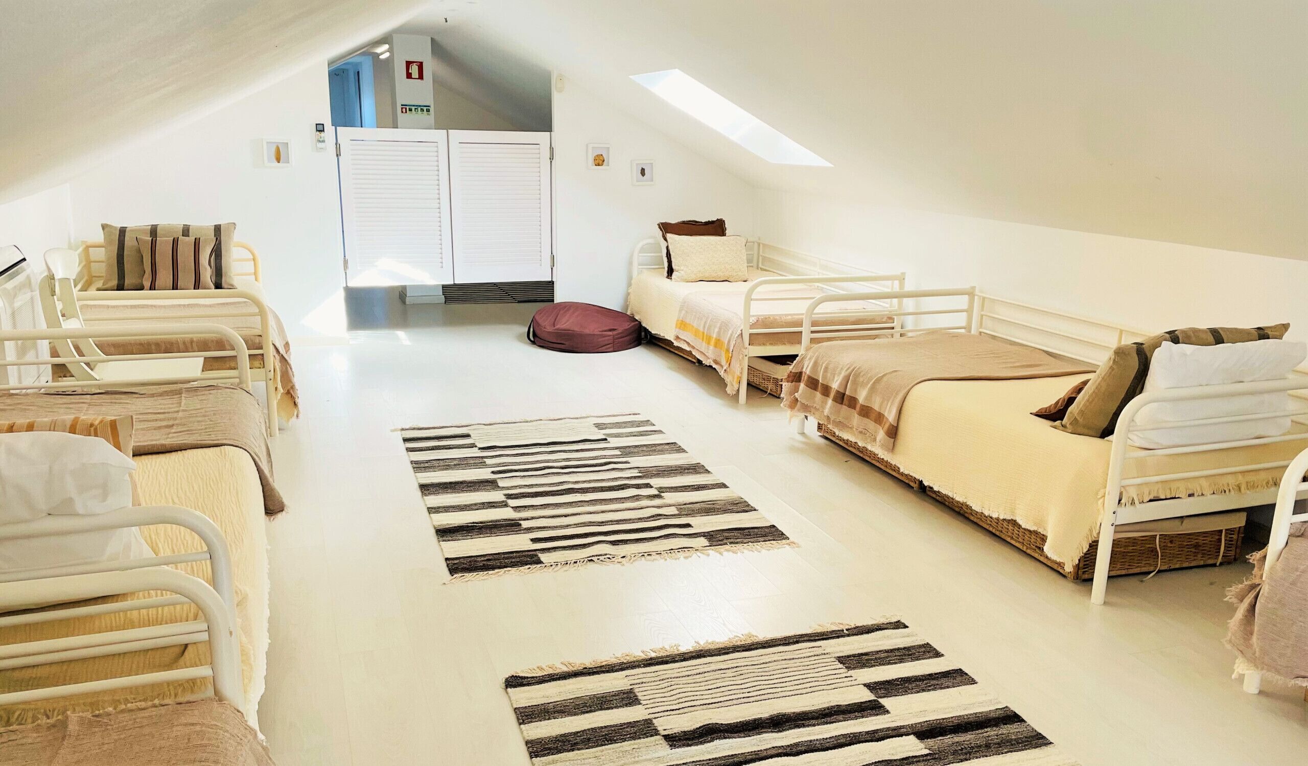 A dormitory room with bunk beds, a skylight, a fire alarm, and a white door.