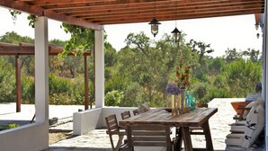 Patio esterno con tavolo e sedie di legno, circondato da pareti bianche e una pergola.