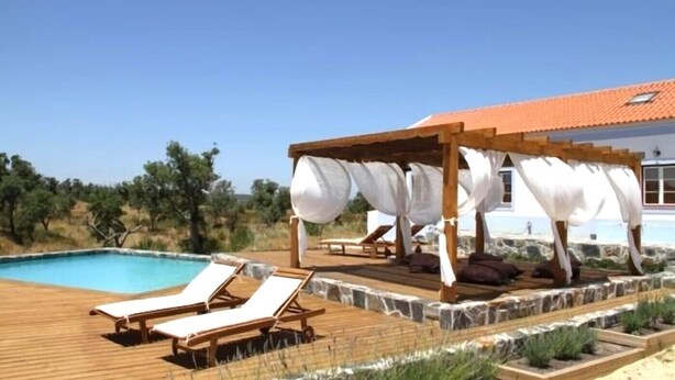 Area piscina con lettini e una pergola corredata di tende bianche.