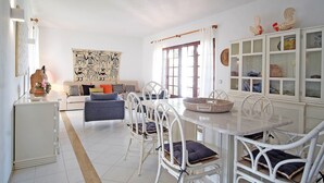 A dining area with a white table and chairs, a sofa, and a cabinet with glass doors. - VV Beautiful Villa w/pool | A/C | VILAMOURA! (Quarteira)