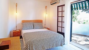 A bedroom with a bed, bedside tables, a hanging light, an air conditioning unit, and a view of the outdoors through a door. - VV Beautiful Villa w/pool | A/C | VILAMOURA! (Quarteira)