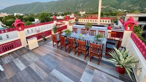 A rooftop terrace with a dining area, potted plants, and a view of a hill with a monument. - Hotel Mitra Inn (Pushkar)