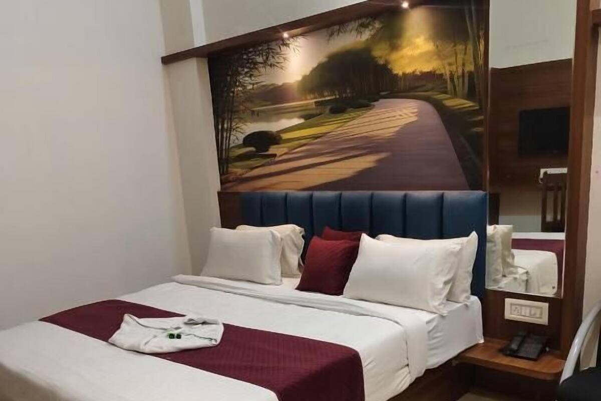 Una camera d'albergo con un letto grande, una testiera decorata con un dipinto, un comodino e una poltrona.