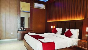 A hotel room with a large bed, wooden panel walls, a mirror, an air conditioning unit, and a bedside table with a lamp. - Hotel Mitra Inn (Pushkar)