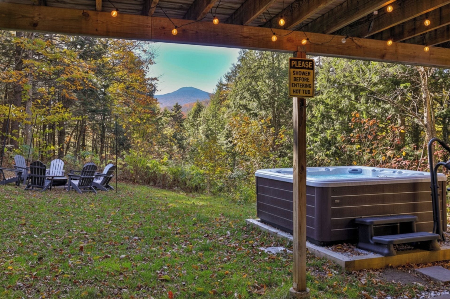 Un bain à remous installé sous une pergola en bois, avec un panneau indiquant qu’il faut prendre une douche avant d’y entrer.