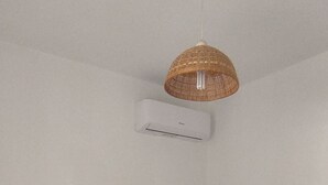 A neatly made bed with two rolled towels, a woven light fixture, and a wall-mounted air conditioner. - Beachfront apartment with panoramic view (San Lorenzo)