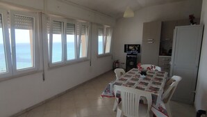 A dining area with a table set for four, large windows with ocean views, and a kitchen area with cabinets and a refrigerator. - Beachfront apartment with panoramic view (San Lorenzo)