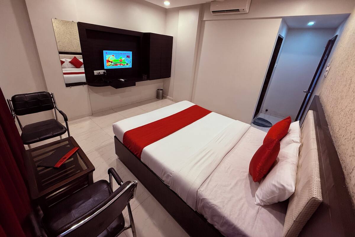 Habitación de hotel con cama, televisor montado en la pared, una silla y escritorio.