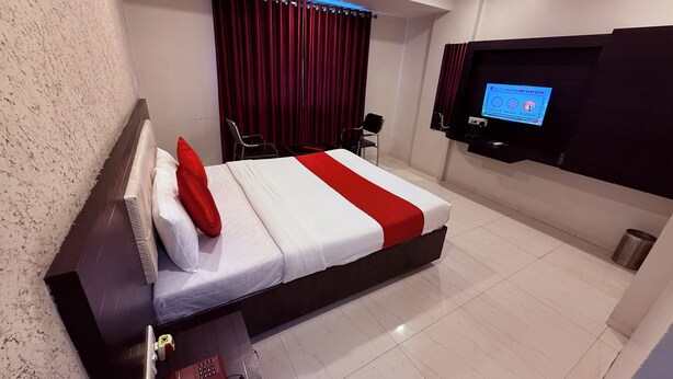 A hotel room with a large bed, a TV mounted on the wall, a desk with a telephone, and a chair. - Hotel Arya Residency Rabale (Navi Mumbai)
