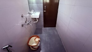 A narrow bathroom with a white sink, a mirror, and a shower. - Hotel Arya Residency Rabale (Navi Mumbai)