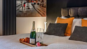 Un lit avec une bouteille de champagne, des verres et des croissants sur un plateau, des oreillers et un tableau encadré au mur.