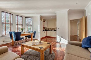 A modern living room with a dining area, kitchen, and a view of the outdoors through large windows. - The Milton Smart Spacious 3-Bed Bournemouth (Bournemouth)