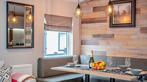 Een moderne eetruimte met een houten wand, een bank, een tafel gedekt voor twee personen en hanglampen.