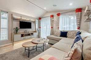 Ein modernes Wohnzimmer mit einer Couch, einem Fernseher, einem Couchtisch und Vorhängen.