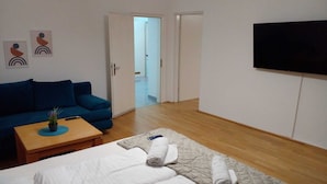Ett hotellrum med en blå soffa, ett träbord, en säng med vita sängkläder och en tv som är monterad på väggen.