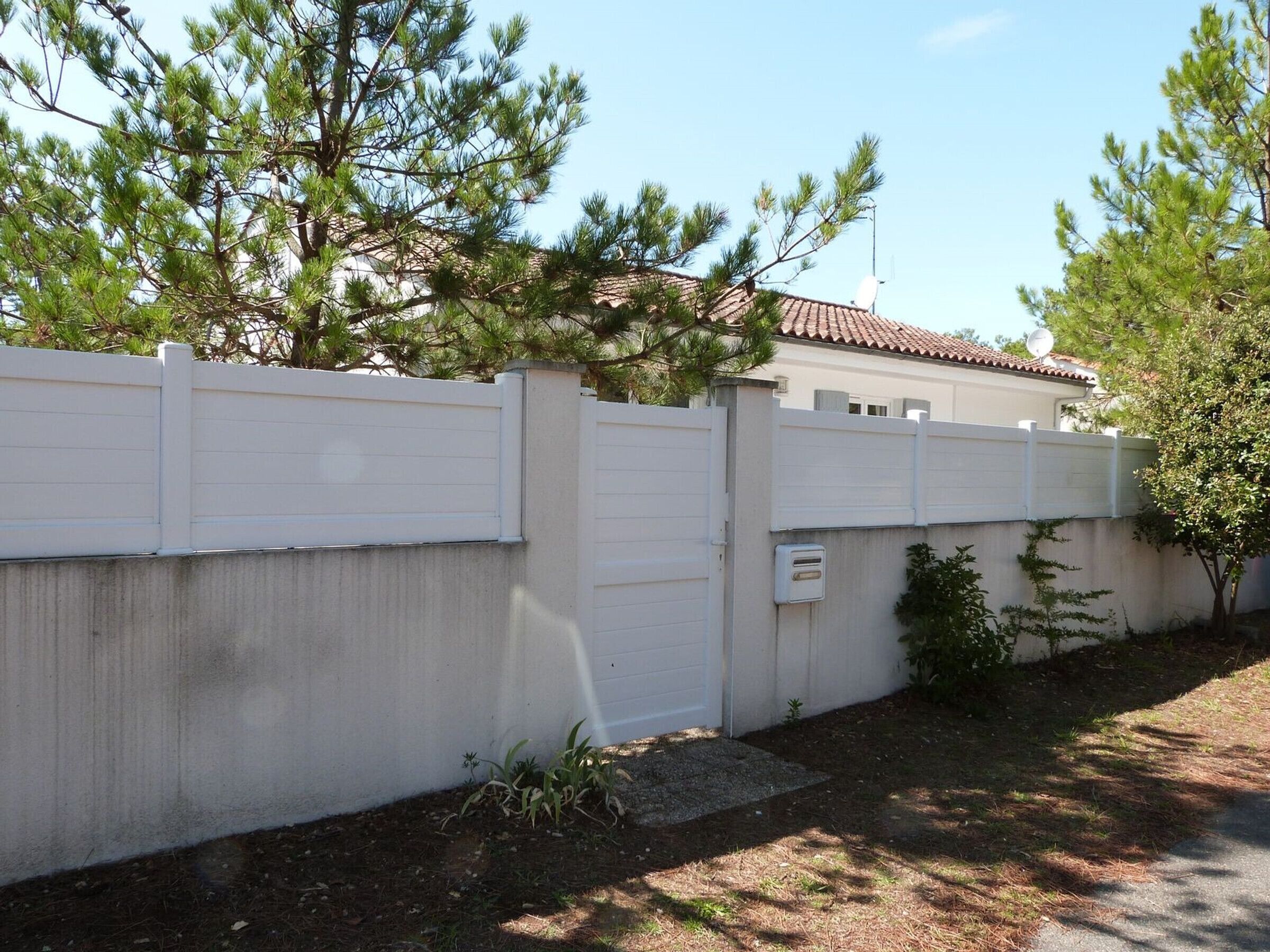 Un quartier résidentiel avec une clôture blanche, un mur en béton et une maison avec un toit en tuiles.