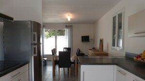 Een moderne keuken met een koelkast, een eethoek met stoelen, een tafel en een schaal fruit.