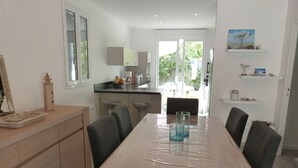 Een moderne keuken met een centraal eiland, een eethoek met een tafel en een uitzicht op het buitengebied via een schuifdeur.