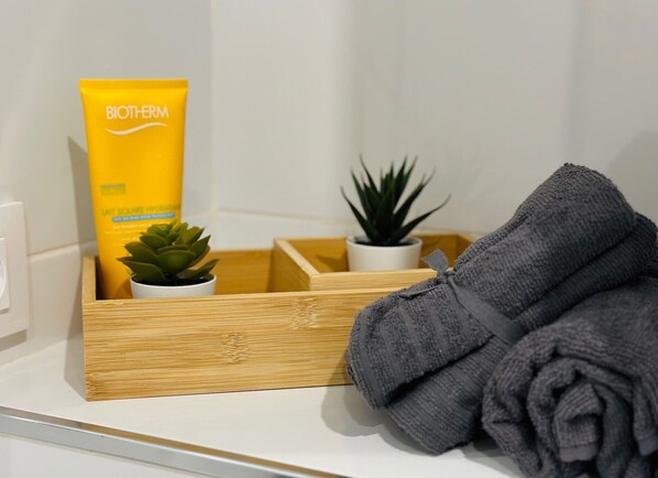Een badkamer met een houten dienblad waarop een tube Biotherm lotion, een kleine potplant en een opgerolde handdoek staan.