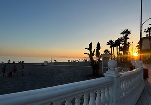 Een strand met een witte balustrade, palmbomen en een zonsondergang.