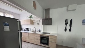 Una cocina moderna con armarios de madera clara, horno empotrado, pileta y estufa. Hay una planta en maceta sobre la encimera y un juego de cuchillos colgado en la pared.