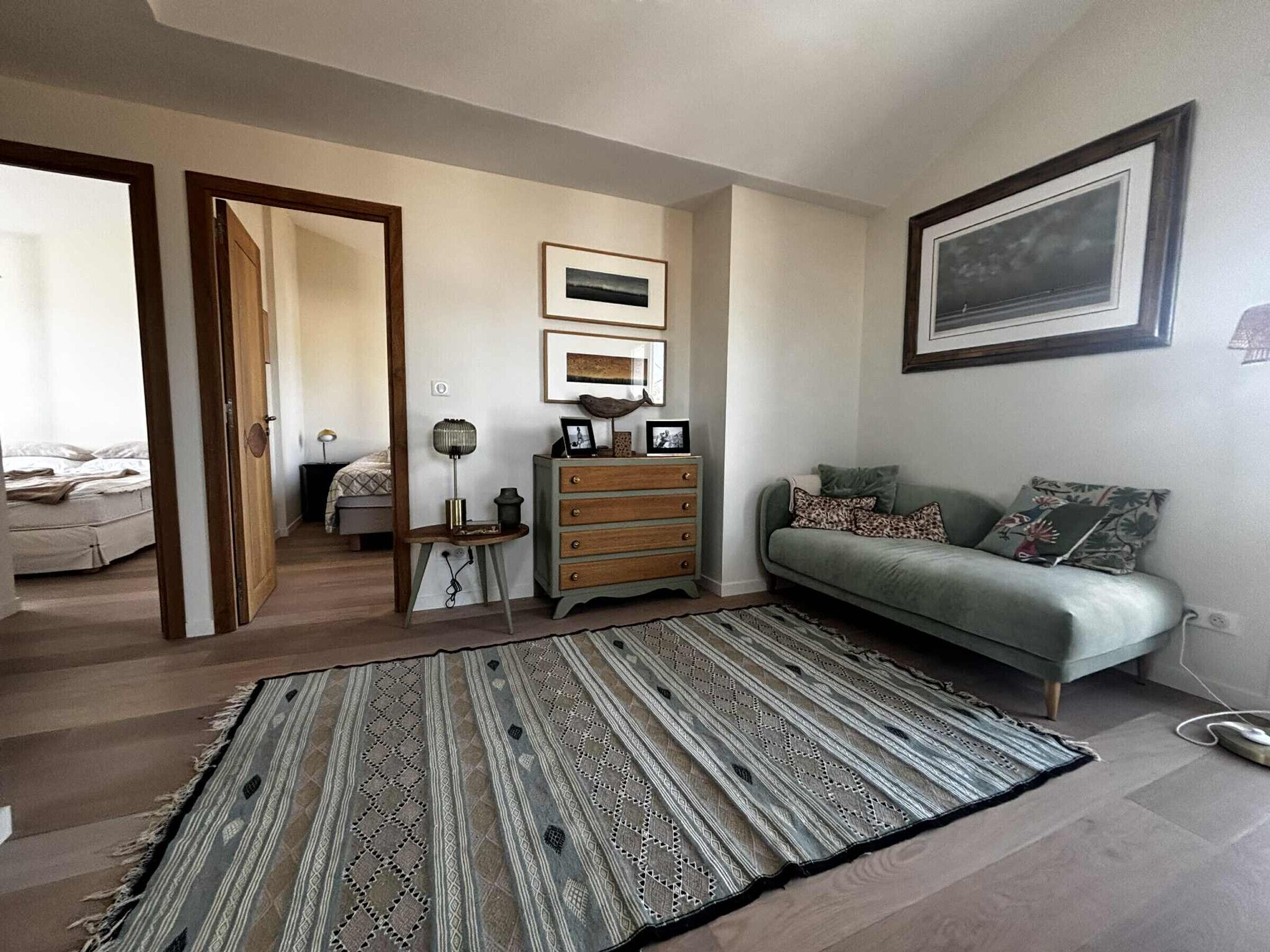 A living room with a sofa, a patterned rug, a wooden dresser, and framed artwork on the walls.