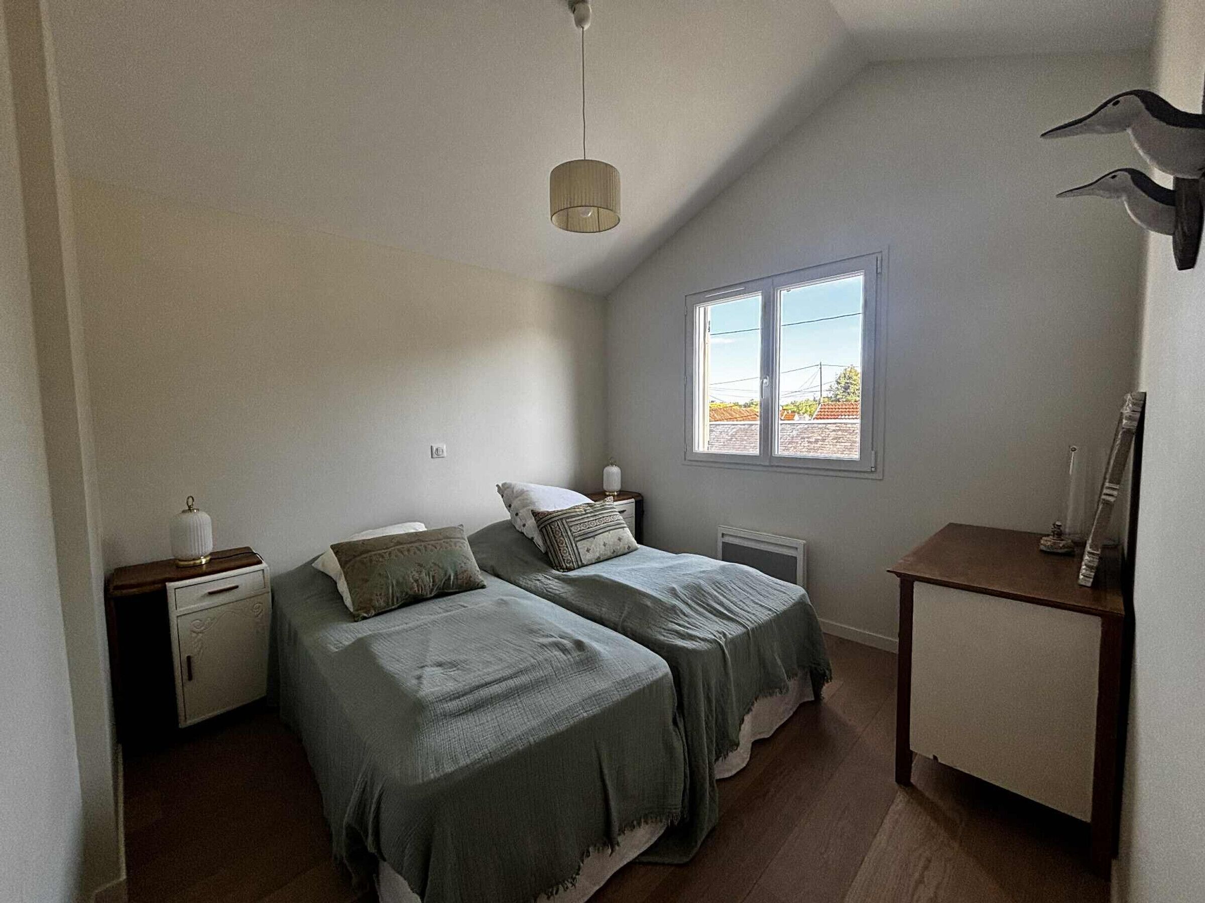 Un dormitorio con dos camas, una ventana, una mesita de noche y un aparador.