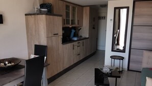 A modern kitchen with wooden cabinets, a dining area with a black table and chairs, and a small side table with glasses.