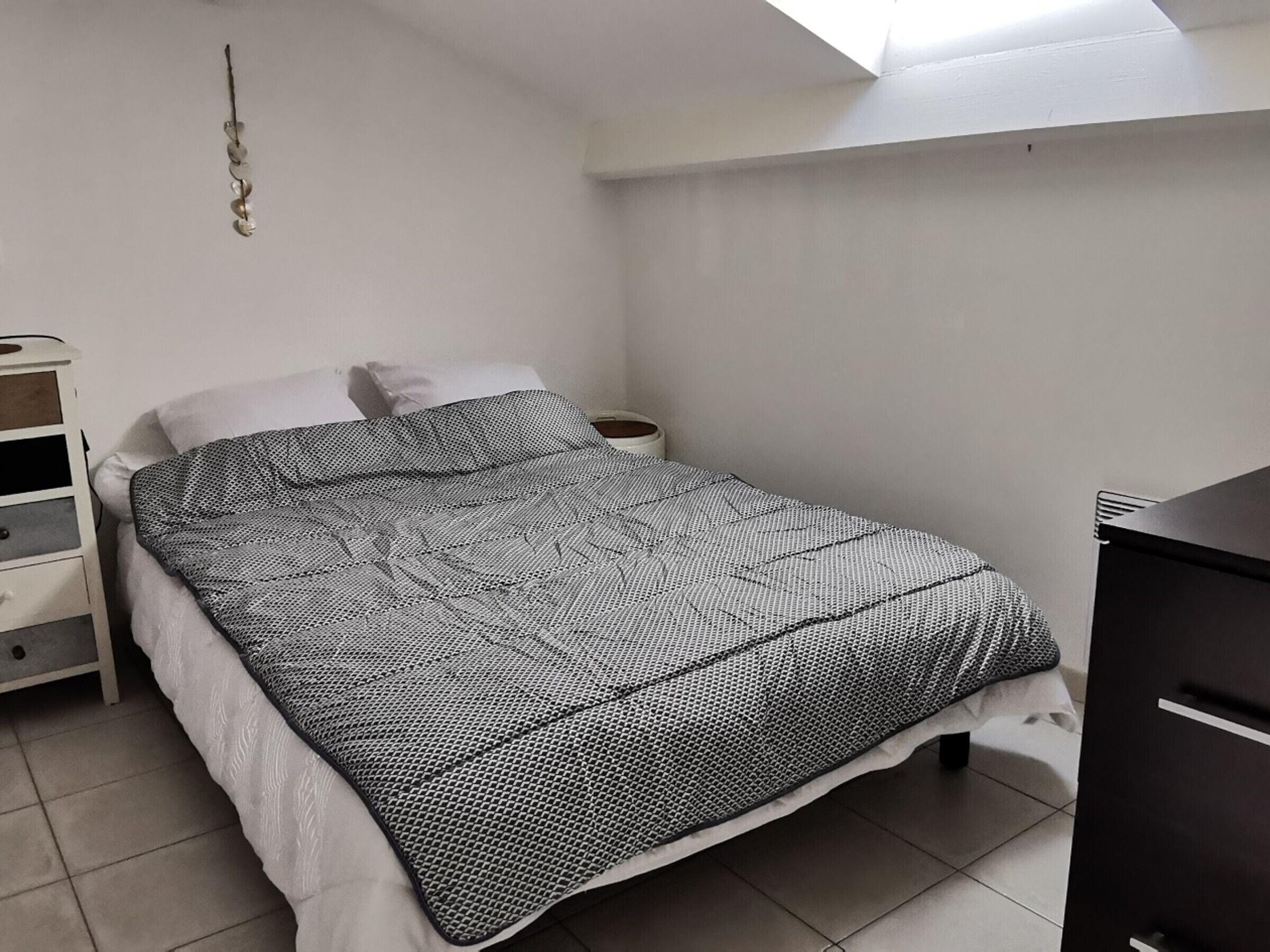 Quarto com cama, cômoda, mesa de cabeceira e luminária suspensa.