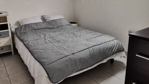 A bedroom with a bed, a dresser, a nightstand, and a hanging light fixture.