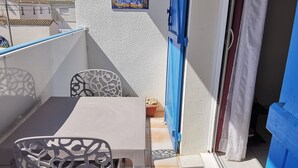 A balcony with a white table and chairs, a blue door, and a tiled floor.