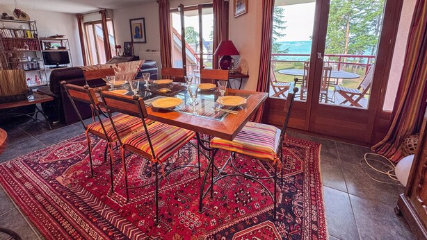 A dining area with a table set for six, surrounded by chairs, a patterned rug, and a chandelier. - Duplex with Terrace and Private Beach Access, Garage Included (Évian-les-Bains)