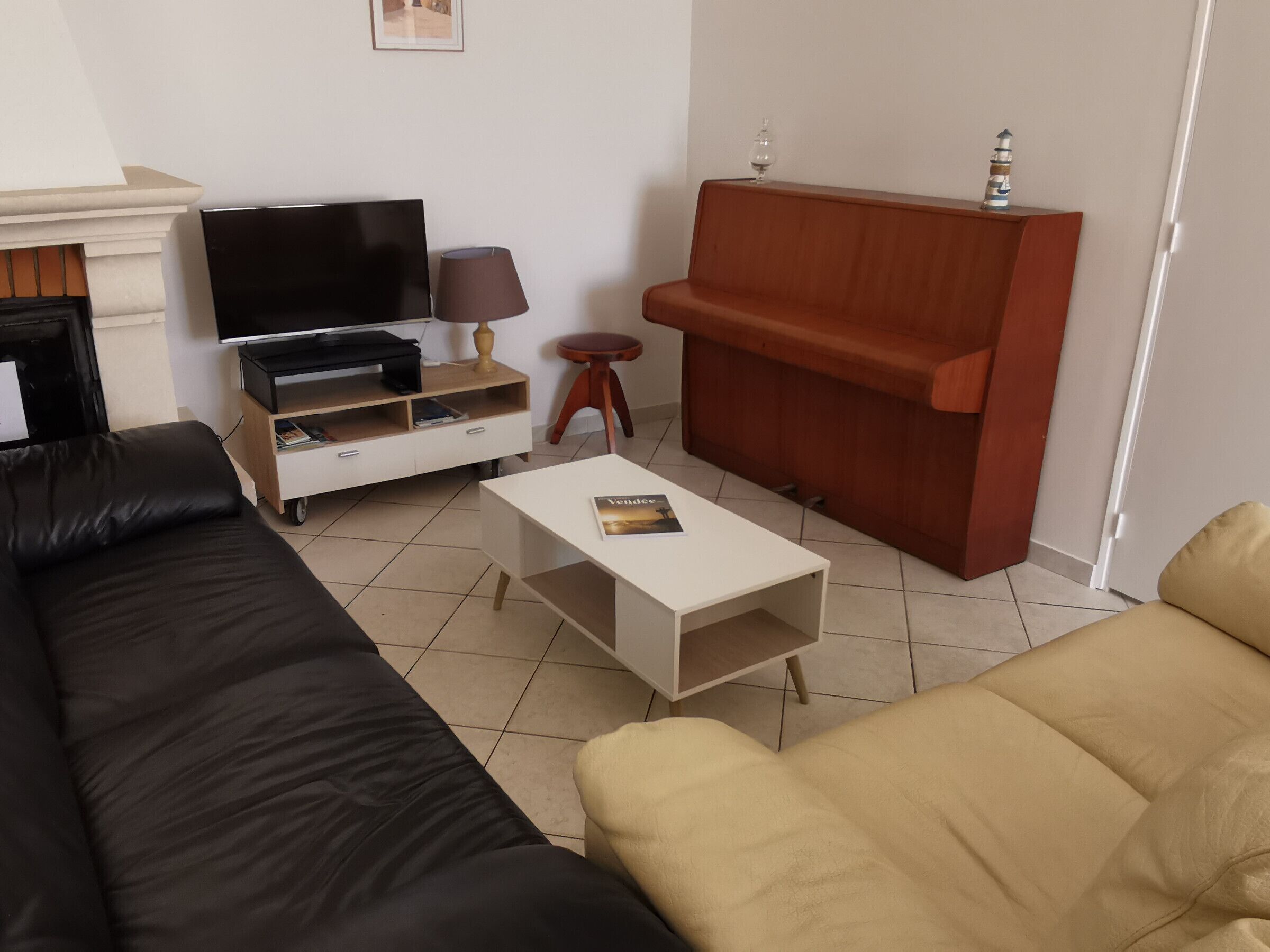 Un salon avec un canapé noir et beige, une table basse blanche, un meuble TV avec un téléviseur à écran plat, une lampe et un meuble de rangement en bois.