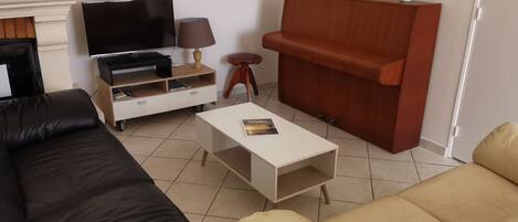 Un salon avec un canapé noir et beige, une table basse blanche, un meuble TV avec un téléviseur à écran plat, une lampe et un meuble de rangement en bois.