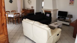 Ett vardagsrum med en soffa, TV, öppen spis, matbord, stolar och ett träskåp.