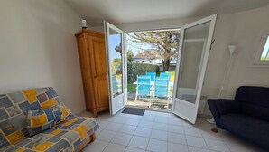 A living room with a sofa, a blue couch, a wooden cabinet, and a sliding glass door leading to an outdoor area with chairs and a table. - House near beach and downtown La Faute-sur-Mer (La Faute-sur-Mer)