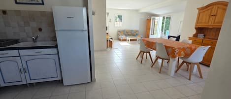 A kitchen with a refrigerator, a dining area with a table and chairs, and a sofa in the background.