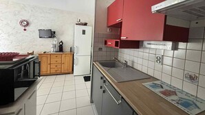 A compact kitchen with a refrigerator, microwave, and wooden cabinets. - Cozy city-center apartment, 400m from beaches, parking included (La Tranche-sur-Mer)
