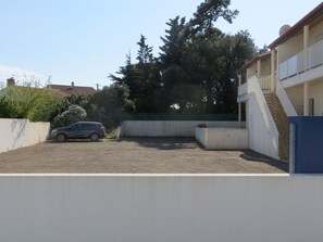 A parking area with a car, a building with a staircase, and trees in the background. - Cozy city-center apartment, 400m from beaches, parking included (La Tranche-sur-Mer)