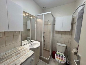 A bathroom with a wooden vanity, a white sink, a mirror, a shower enclosure, and a toilet with a colorful seat. - Cozy city-center apartment, 400m from beaches, parking included (La Tranche-sur-Mer)