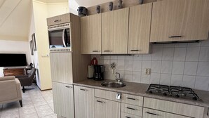 Ett kompakt kök med ljusa träskåp, en inbyggd mikrovågsugn, en gasspis och ett diskho.