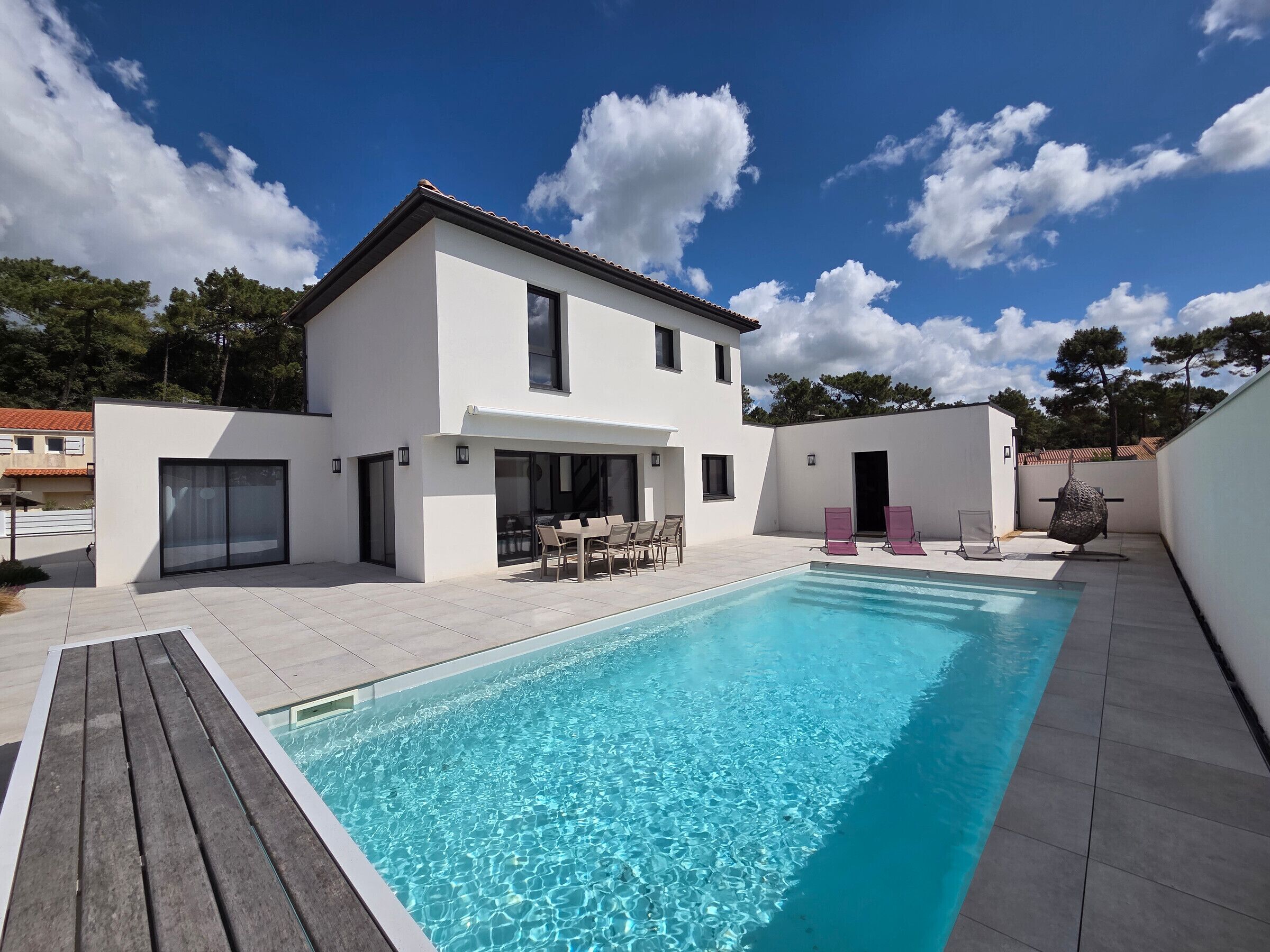 Une maison moderne à deux étages, dotée d’une piscine, d’un espace extérieur aménagé et surplombant un ciel d’un bleu limpide.