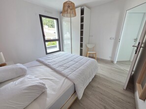 Ein Schlafzimmer mit Bett, Fenster, Sessel und Kleiderschrank.